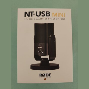 Fotografie znázorňuje produktový manuál nebo obal k mikrofonu. Je na něm zobrazen černý kondenzátorový mikrofon na stojanu s nápisy NT-USB MINI a STU…