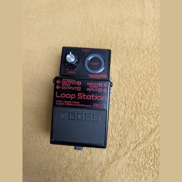 Černý efekt pedál značky BOSS s nápisem Loop Station a označením modelu RC-1. Horní panel obsahuje ovládací knob LEVEL, červené tlačítko LOOP a tlačí…