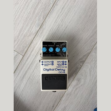 Kytarový efekt Boss Digital Delay DD-8 v bílém provedení. Na horní části jsou čtyři modré ovládací knoflíky s popisky E.LEVEL, FEEDBACK, TIME a LOOP…