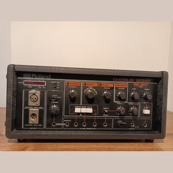 Černý efektový procesor Roland CHORUS ECHO RE-501 v robustním pouzdře. Přední panel obsahuje různé ovládací knofíky, přepínače a vstupní/výstupní kon…