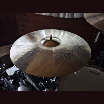 Zlatavý činel s viditelným broušením povrchu. Na pravé straně je nápis istanbul Agop Handmade Turkey. V horní části je vyryto trojúhelníkové logo. Či…