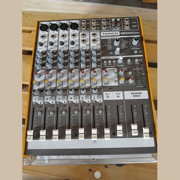 Šedý mixážní pult v oranžovém rámu s nápisem TAPCO MIX220FX. Zařízení obsahuje osm kanálů s posuvníky, různé ovládací knofíky a sekci INTERNAL EFFECT…