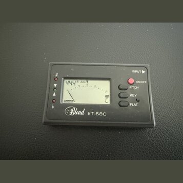 Černý digitální ladicí přístroj s LCD displejem. Na spodní straně je bílý nápis Blond ET-68C. Vpravo se nachází červené tlačítko ON/OFF a tři oválná…