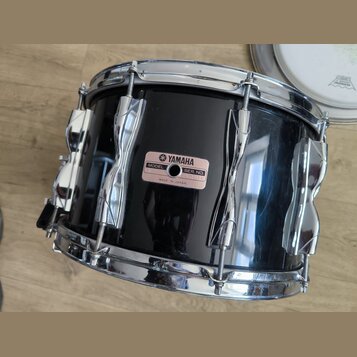 Černý buben s chromovanými obručemi a lugy. Na korpusu je nalepený růžový štítek s nápisy YAMAHA, MODEL, SER. NO. a MADE IN JAPAN. Povrch korpusu vyk…