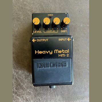 Černý efekt pedál s nápisy Heavy Metal a HM-2. Horní část obsahuje čtyři žluté ovládací knoflíky s popisky LEVEL, COLOR MIX (označený L a H) a DIST.…