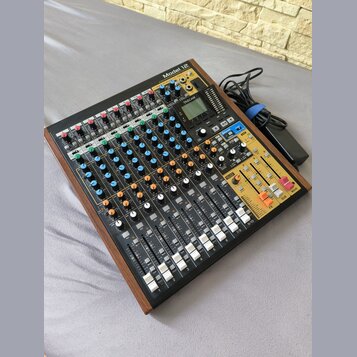Míchací pult Model 12 značky TASCAM v černém provedení s dřevěnými bočními panely. Zařízení obsahuje více vstupních kanálů s řadou potenciometrů, pře…