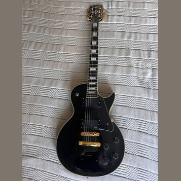 Černá elektrická kytara s gold hardwarem a bílými blokovými vložkami na hmatníku. Na hlavě je nápis Epiphone a logo, na snímači je vidět nápis Epipho…
