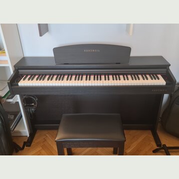 Černý digitální piano v černém dřevěném korpusu s přívodní stoličkou v odpovídající barvě. Na horní části krytu i v pravém dolním rohu je bílý nápis…