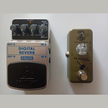 Dvě kytarové efektové pedály z ptačí perspektivy. Levý je stříbrný s černým spínacím pedálem a nápisy DIGITAL REVERB, DR600 a behringer. Má tři ovlád…