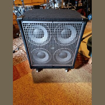 Černý basový reproduktor v bedně potažené texturou. Přední strana je kryta kovovou mřížkou, za kterou jsou vidět čtyři šedé reproduktory. Bedna stojí…