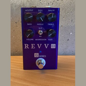 Modrý kytarový efekt pedál s kovovým povrchem. Na přední straně jsou šest černých otočných ovladačů s popisky BASS, MIDDLE, TREBLE, VOLUME, GAIN a př…