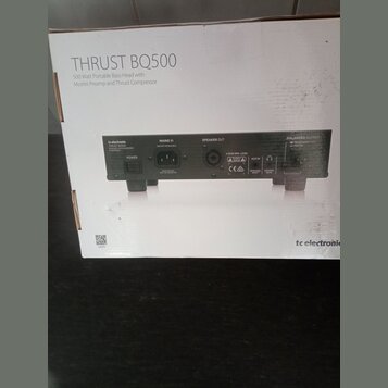 Fotografie zachycuje kartonovou krabici s černým basovým kombem. Na krabici je nápis THRUST BQ500 a text 500 Watt Portable Bass Head with Mosfet Prea…