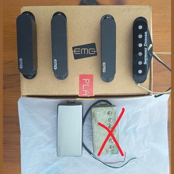Na kartonové krabici s logem EMG leží čtyři snímače k elektrické kytáře. Tři z nich jsou černé s nápisem EMG a jeden je černý s nápisem Seymour Dunca…
