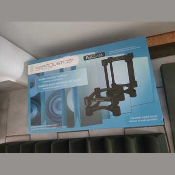 Fotografie znázorňuje krabici s produktem značky ISOACOUSTICS, na které je nápis „Sound quality by design“ a označení modelu ISO-155. Na obalu je tex…