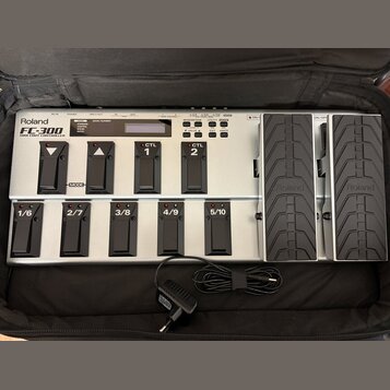 Stříbrný MIDI pedál s černými spínači a dvěma expresními pedály. Na zařízení je nápis Roland FC-300 MIDI FOOT CONTROLLER a na expresních pedálech log…