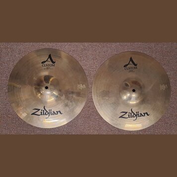 Dvě mosazné činely značky Zildjian. Levý činel nese nápisy A CUSTOM a HIHAT BOTTOM 14" 35,56 cm. Pravý činel má nápisy A CUSTOM a HIHAT TOP 14" 35,56…