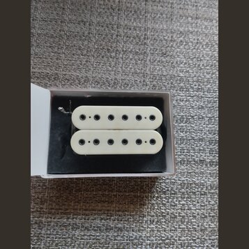 Dvě bílé humbucker snímače s šesti viditelnými póly umístěné v bílé krabičce na černém polstrování. Na snímačích nejsou žádné viditelné značky, loga…
