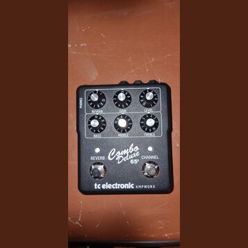Černý kytarový předzesilovač s bílým předním panelem. Na panelu jsou šest otočných ovladačů s popisky REVERB, GAIN, LEVEL, BASS, MIDDLE a TREBLE, dva…