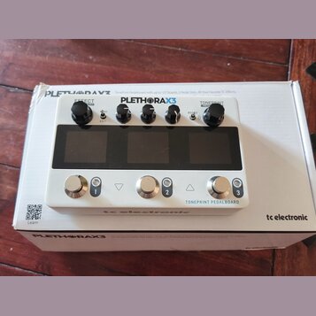 Bílý efektový pedál s nápisem PLETHORA X3 a TONEPRINT PEDALBOARD. Na horní části jsou čtyři černé ovládací knoflíky a tři velké černé spínače s nápis…