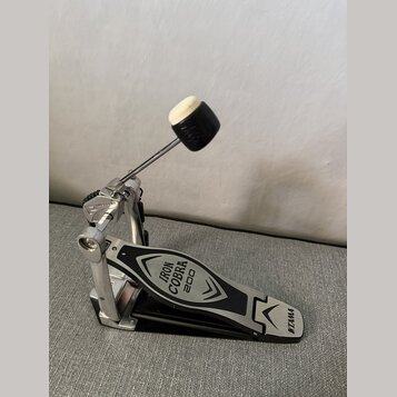 Stříbrný basový pedál s černým šlapadlem. Na šlapadle jsou nápisy IRON COBRA 200 a logo TAMA. Povrch vykazuje mírné známky používání v podobě drobnýc…
