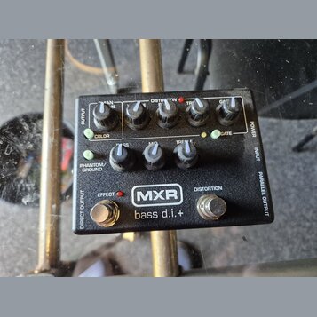 Černý kytarový pedál s nápisy MXR a bass d.i.+ . Zařízení obsahuje pět otočných potenciometrů s popisky BASS, MID, TREBLE, GAIN a GATE, dva zapínací…