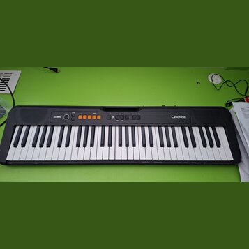 Černý elektronický klavír s bílými a černými klávesami. Na levé straně je bílé logo CASIO a na pravé straně nápis CasioTone CT-S100. V horní části se…