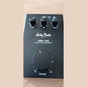 Černý kytarový výkonový zesilovač s nápisy Harley Benton, GPA-100 a Guitar Power Amplifier. Horní část obsahuje tři menší otočné ovladače s popisky B…