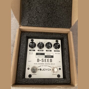 Bílý efekt pedál D-SEED DUAL CHANNEL DIGITAL DELAY značky JOYO v kartonové krabici s pěnovou výplní. Na horní straně jsou čtyři černé ovládací knoflí…