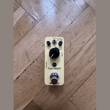 Krémový efekt pedál s nápisy FUNKY MONKEY a MOOG. Na horní straně jsou ovládací prvky: dva malé černé knoflíky u nápisů RANGE a Q, jeden velký černý…