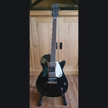 Černá elektrická kytara s tmavým hmatníkem a bílým trsátorem. Na hlavě i na trsátoru je bílý nápis GRETSCH. Nástroj má dva snímače typu humbucker a j…
