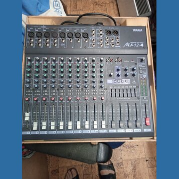Šedý mixážní pult značky YAMAHA, model MX12/4. Zařízení obsahuje několik vstupních kanálů s posuvníky, knoflíky pro gain a ekvalizaci a sekci ST GRAP…