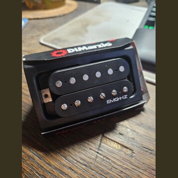 Černý humbucker s dvěma řadami snímačů umístěný v originálním černém obalu. Na spodní části je bílý nápis EMG-HZ a na horní hraně obalu červené logo…
