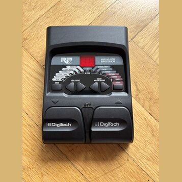 Černý kytarový procesor s nápisy RP 55 a MODELING GUITAR PROCESSOR. Zařízení obsahuje červený digitální displej, několik ovládacích tlačítek a dva pe…