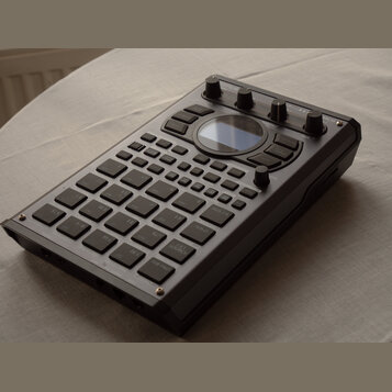 Černý sampler s množstvím gumových padů, tlačítek a ovládacích knoflíků. Na horní hraně je nápis Novation GrooveStation II. Zařízení obsahuje malý di…