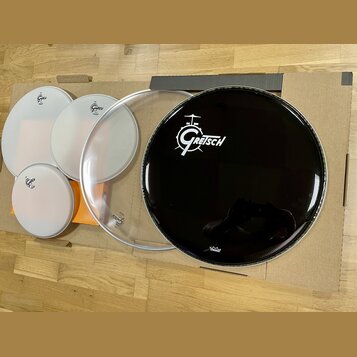 Sada bubenových koží položená na kartonovém podkladu. Na bílých a průhledné kožem jsou viditelná loga Gretsch. Největší černá koža nese bílé logo Gre…