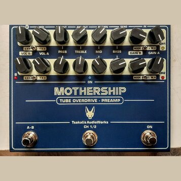 Modrý rackový efekt s nápisy MOTHERSHIP a TUBE OVERDRIVE - PREAMP. Na spodní části je logo s hlavou zvířete a text TsakalisAudioWorks CH 1/2. Zařízen…