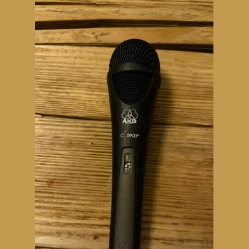 Černý dynamický mikrofon s mřížkou v horní části. Na těle je bílé logo AKG a pod ním nápis C 5900M. V dolní části je viditelný přepínač s nečitelnými…