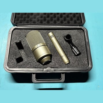 Černý tvrdý kufřík s pěnovou výplní obsahuje zlatavý mikrofon a dopřívodní příslušenství. Na těle mikrofonu je nápis "Cardioid Microphone 991" a logo…