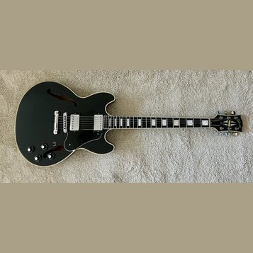 Černá polodupatá elektrická kytara s bílým lemováním a hnědými f-otvory. Na hlavě je viditelné logo Gibson. Nástroj má dva humbuckery, tři ovládací k…