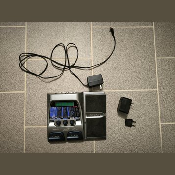 Stříbrný kytarový procesor s černým integrovaným reproduktorem. Na přístroji jsou nápisy "Contax", "RP200" a dvakrát "DigiTech". Součástí je napájecí…