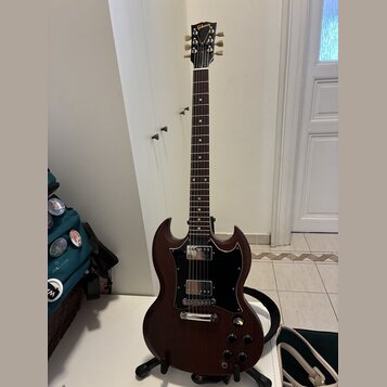 Tmavně hnědá elektrická kytara s dvojsečným tvaru těla a černým pickguardem. Na hlavě hmatníku je zlaté logo Gibson. Nástroj má dva humbuckery, stříb…