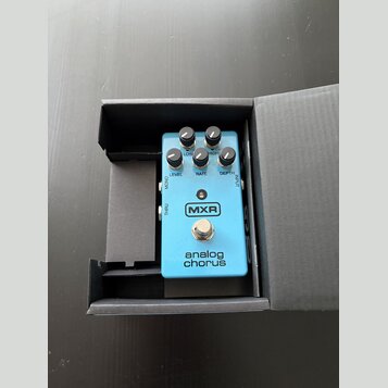 Modrý efekt pedál v černé krabici. Na zařízení je bílé logo MXR a nápis analog chorus. Pedál má pět ovládacích knoflíků s popisky LEVEL, RATE, DEPTH,…
