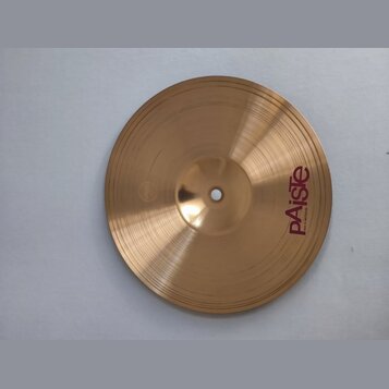 Kruhový činel z mosazného kovu s jemným rýhováním. Na povrchu je vpravo viditelné červené logo Paiste a pod ním menší nápis MADE IN SWITZERLAND. Povr…