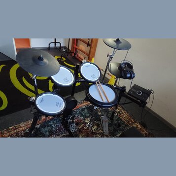 Elektronická bicí souprava značky Roland s bílými padovými plochami a černými činely. Na padech jsou viditelné nápisy Roland a V-Drums. Součástí je č…