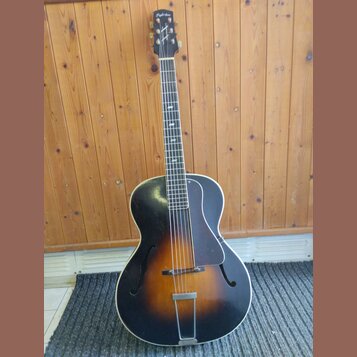 Polodublová elektrická kytara s černým přechodem do hnědé barvy (sunburst) a dvěma f-otvory. Na hlavě hmatníku je bílý nápis „Dygtone“ a logo ve tvar…