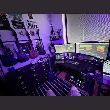 Fotografie zachycuje hudební studio s několika elektrickými kytarami. Na stěně jsou zavěšeny čtyři kytary, z nichž tři jsou černé a jedna červená; na…