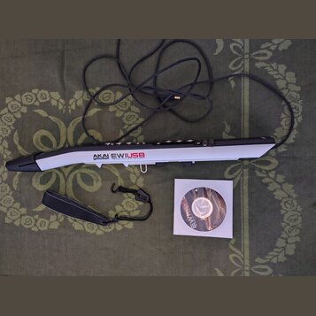 Na fotografii je elektronický dechový nástroj v stříbrno-černé barvě s nápisem AKAI professional EWIUSB USB ELECTRONIC WIND INSTRUMENT. Součástí sady…