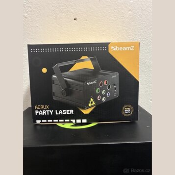 Fotografie znázorňuje kartónové balení laserového efektu. Na krabici je zobrazen černý přístroj s rukojetí a nápisy beamZ, ACRUX a PARTY LASER. V pra…