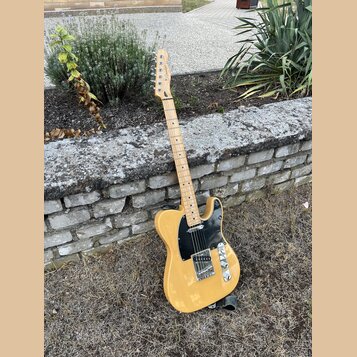 Elektrická kytara typu Telecaster v žlutém provedení s černým pickguardem. Na hlavě hmatníku je viditelné logo Squier. Nástroj vykazuje známky použív…