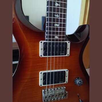 Elektrická kytara s hnědým lakovaným povrchem s viditelnou strukturou dřeva. Nástroj má dva snímače typu humbucker s bílými rámečky, na kterých je uv…
